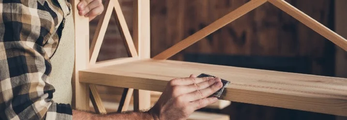 Person schleift Holzbrett mit Schleifpapier